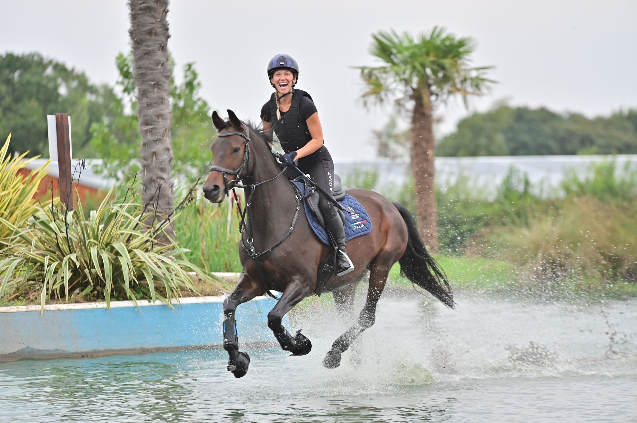 Rider galloping horse through water and smiling.